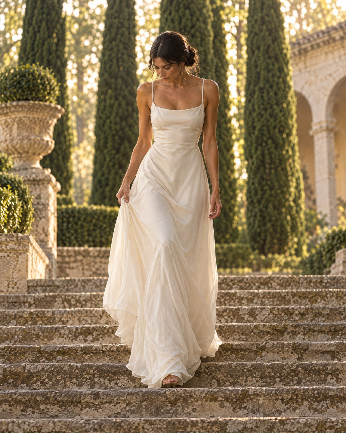 Woman in a flowing ivory maxi dress walking down stone garden steps