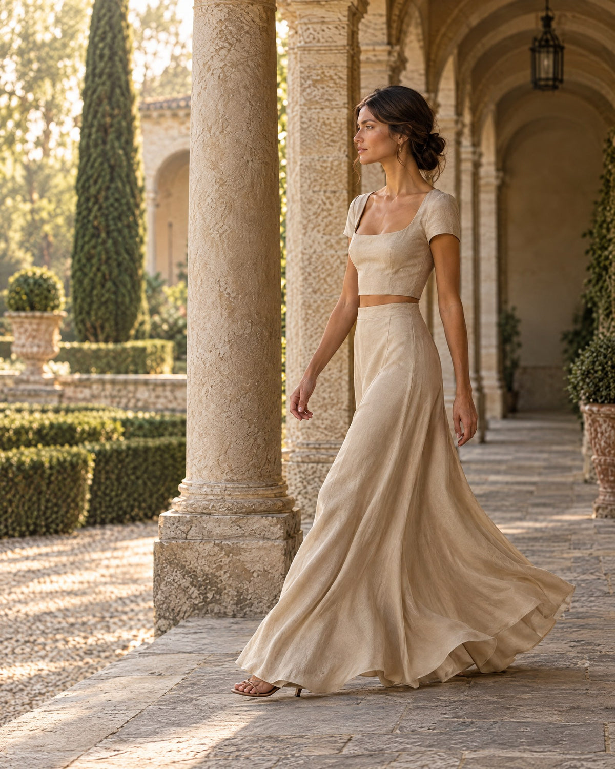Woman in a sand-colored cropped top and long skirt set walking through a colonnade